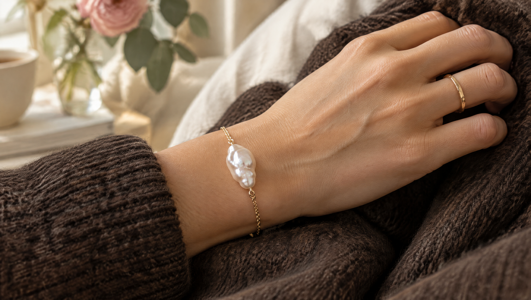 Bracelet chaîne dorée orné d'une perle baroque au poignet d'une femme, sur une maille chocolat
