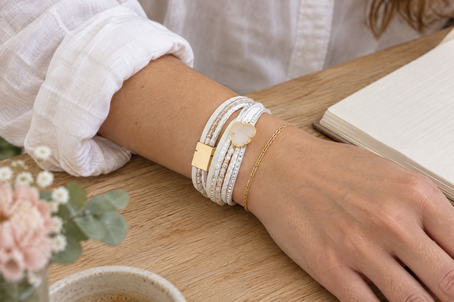 Bracelet blanc à cœur porté avec une fine chaîne dorée sur une chemise en lin
